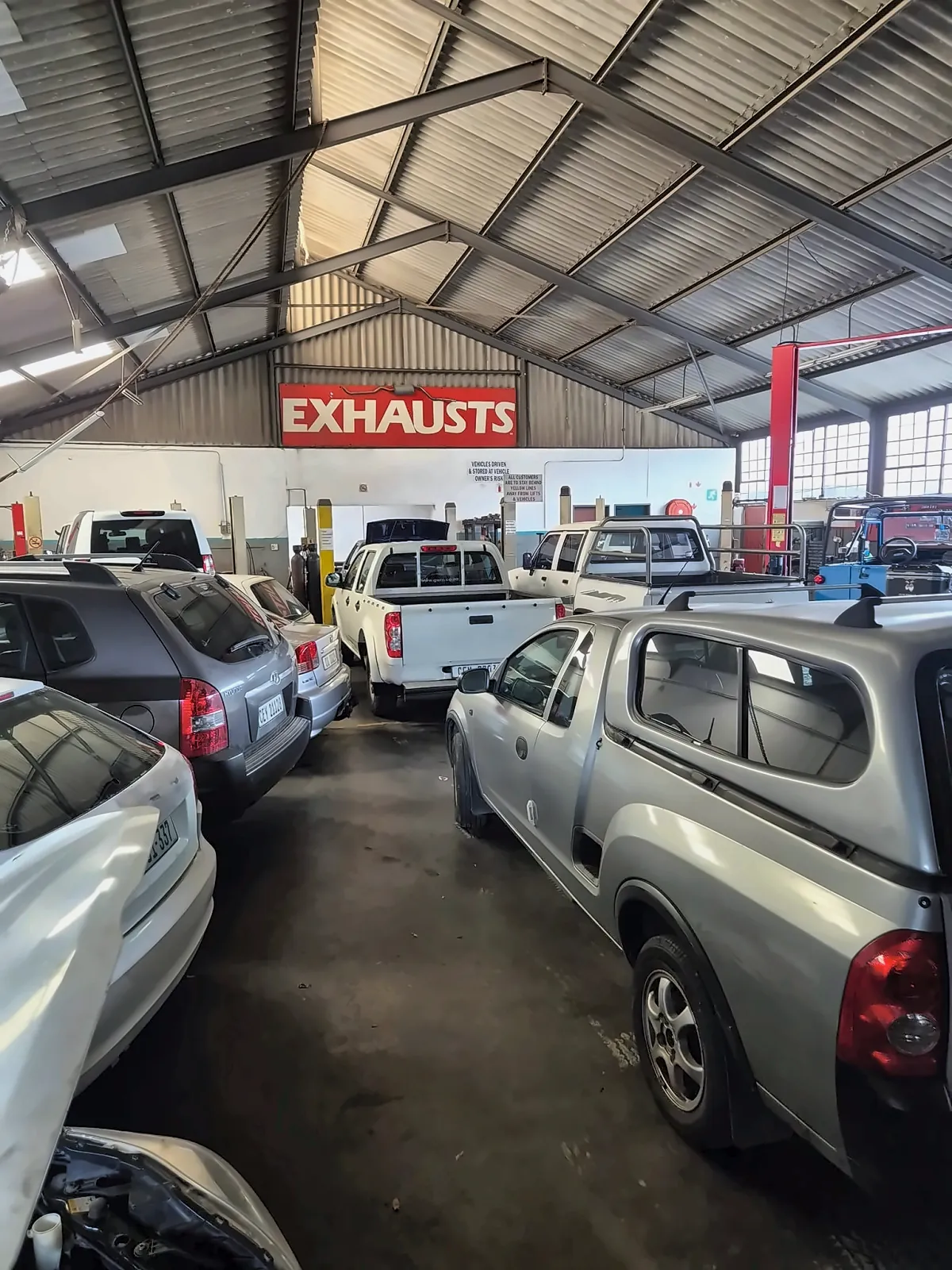 The workshop floor at Muffler Inn, packed nose to tail under the EXHAUSTS sign
